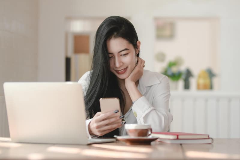 en leende kvinna som sitter och använder en smartphone