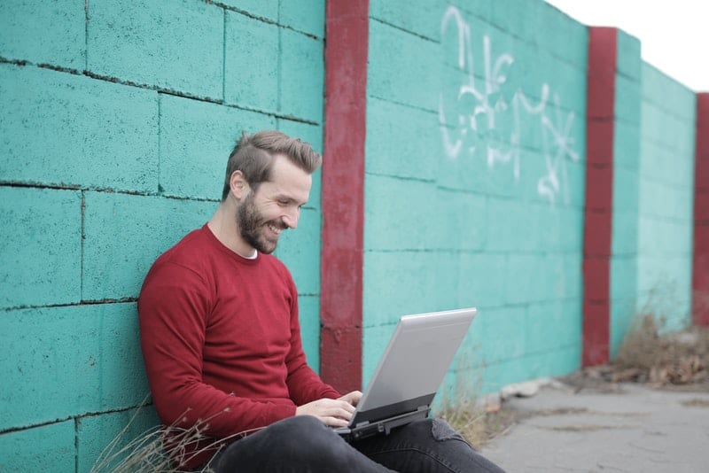 en man i en röd T-shirt sitter och skrattar med en bärbar dator