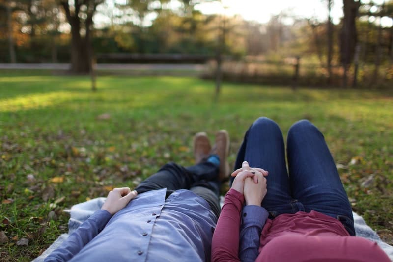 en man och en kvinna ligger i parken och håller händerna