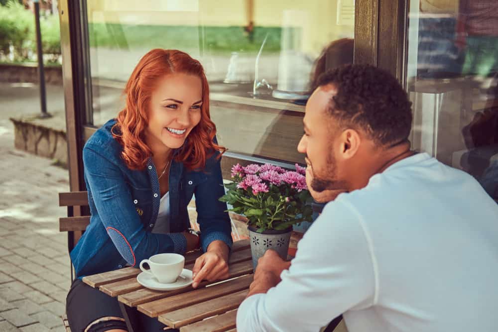 en rödhårig leende flicka som dricker kaffe på terrassen på ett kafé och pratar med en svart man