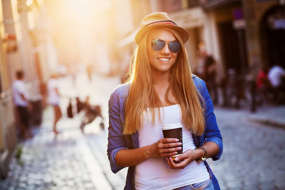 en ung leende blondin med solsken går och dricker kaffe att gå