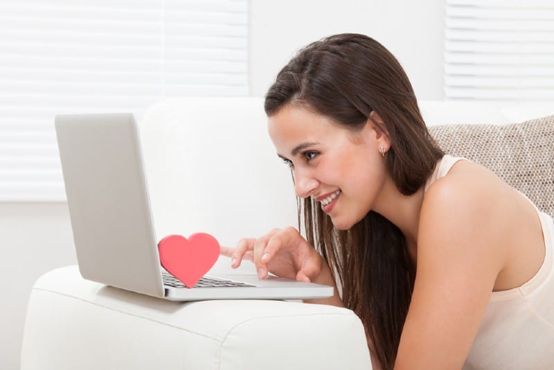 Sidovy av den härliga unga kvinnan som hemma daterar på bärbar dator