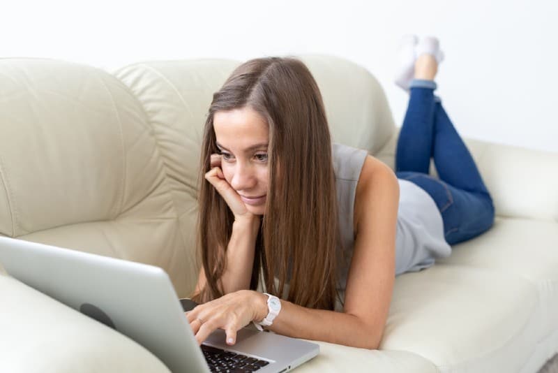 Ung kvinna med bärbara datorn på soffan hemma