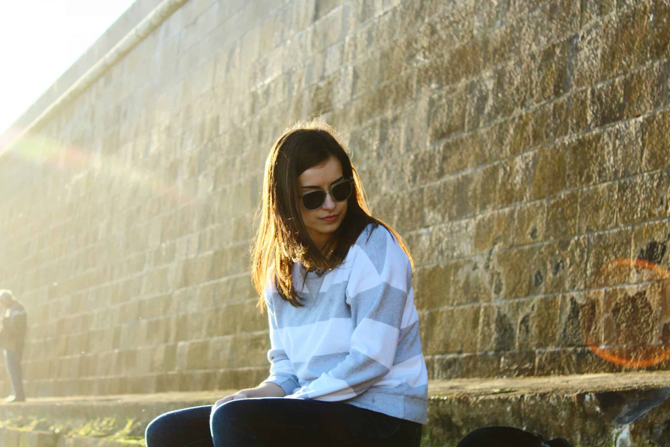 kvinna sitter bredvid väggen med solglasögon