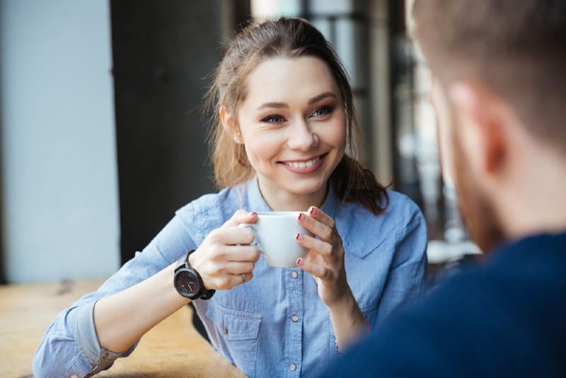 Ung nätt gladlynt kvinna som sitter och dricker kaffe i kafé med den skäggiga mannen