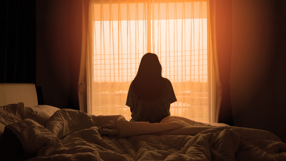 kvinna som sitter på sängen på morgonen med solljus från fönstren