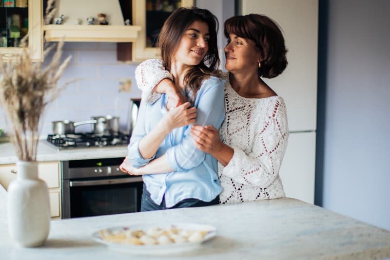 mamma och dotter som står i en omfamning i köket