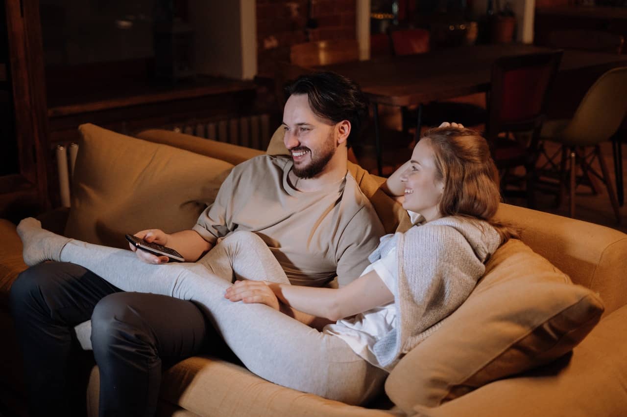 man och kvinna kela på soffan och titta på tv