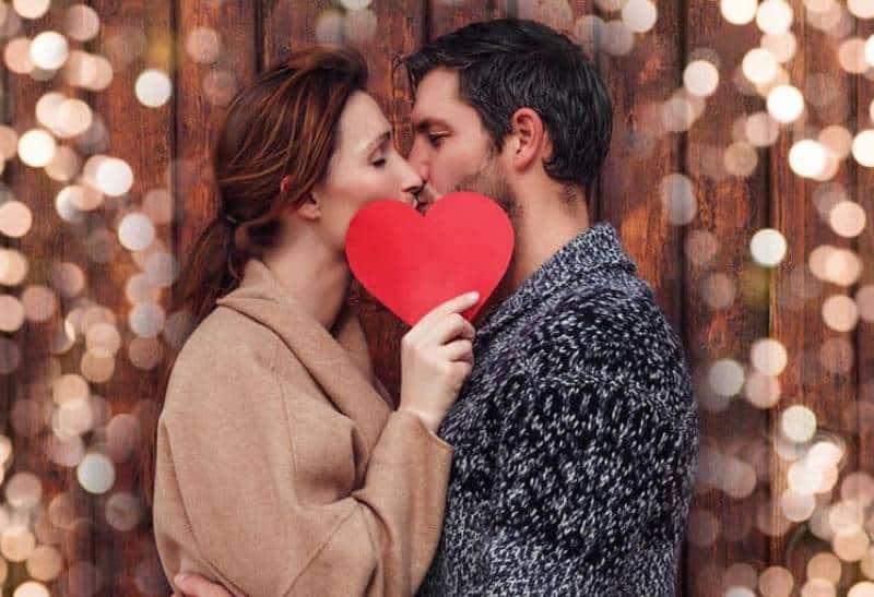 man och kvinna kysser medan kvinna håller pappersform av hjärta