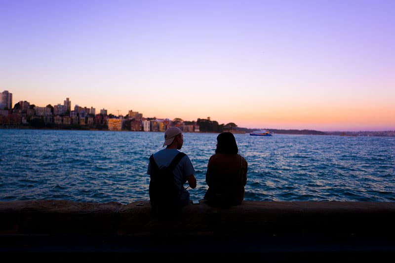 man och kvinna sitter nära vatten och tittar på solnedgången