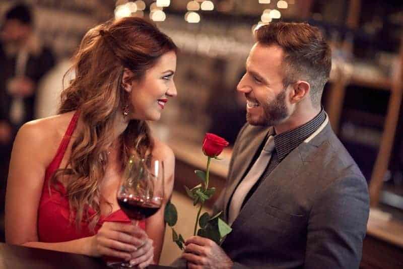 man som håller rosor som står framför kvinnan som håller ett glas och ser varandra