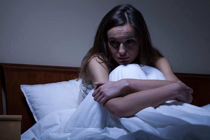 orolig kvinna som sitter under filten i sängen