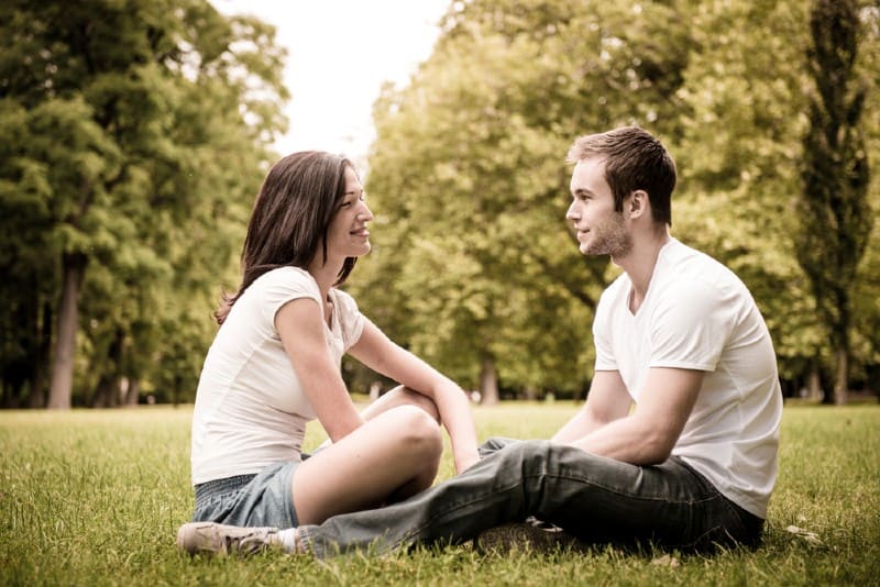 Unga lyckliga par som tillsammans utomhus sitter på gräs