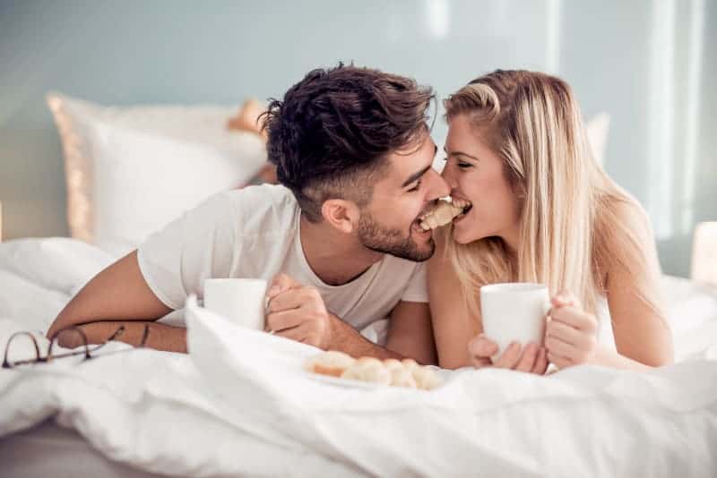 söta par som biter en croissant tillsammans på sängen