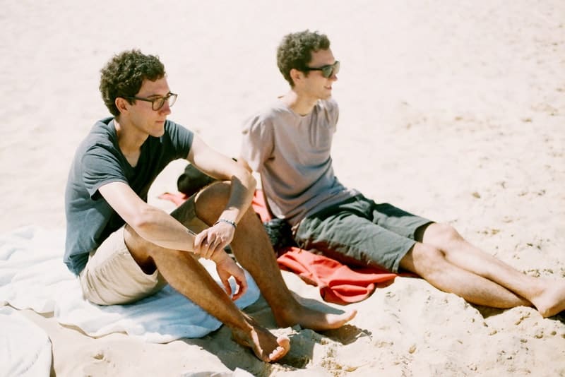 två bröder med glasögon sitter på en sandstrand