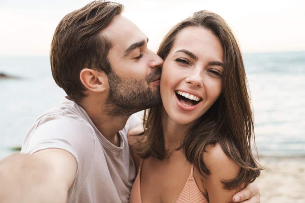 ung glad man som kysser och kramar vacker kvinna medan man tar selfie