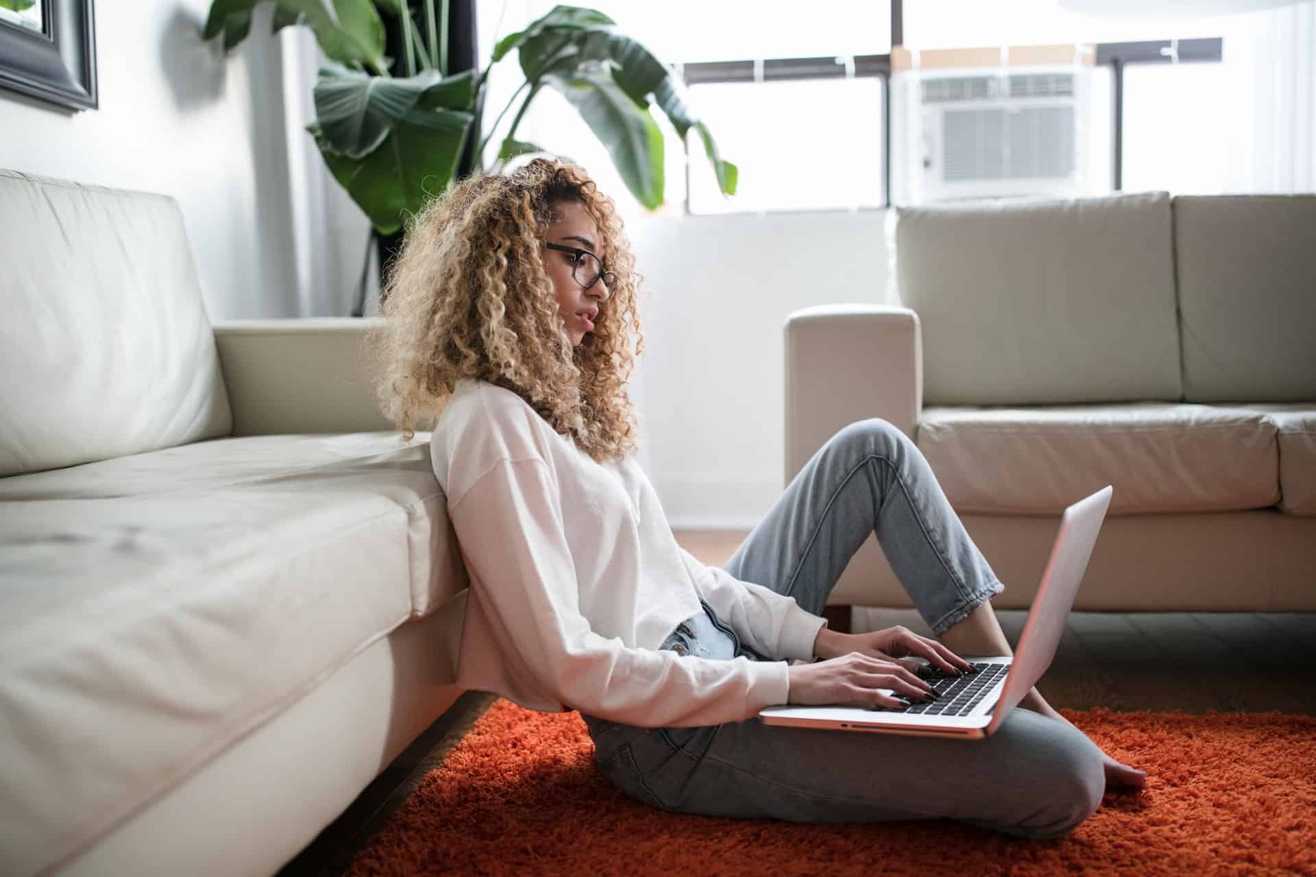 vacker kvinna med lockigt hår sitter på golvet med laptop