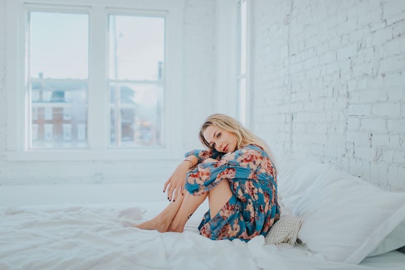 en kvinna i en färgglad klänning sitter böjd på sängen och tänker med ett leende