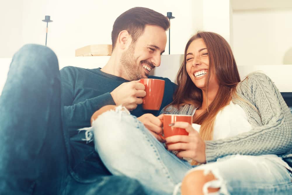 Gladlynt ungt par som hemma dricker kaffe på morgonen