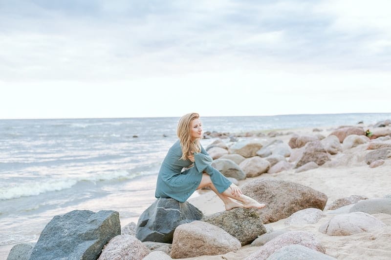 en blondin sitter på en sten på stranden