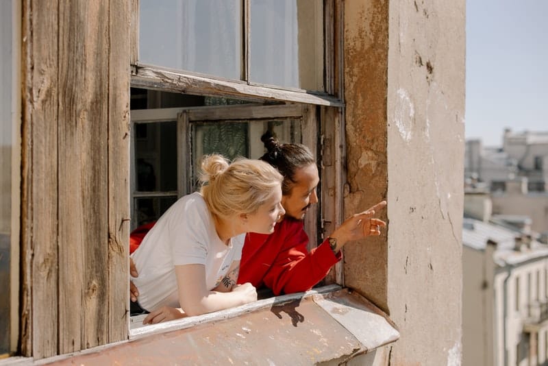 en man i en röd T-shirt står vid fönstret med en kvinna och visar henne något utanför