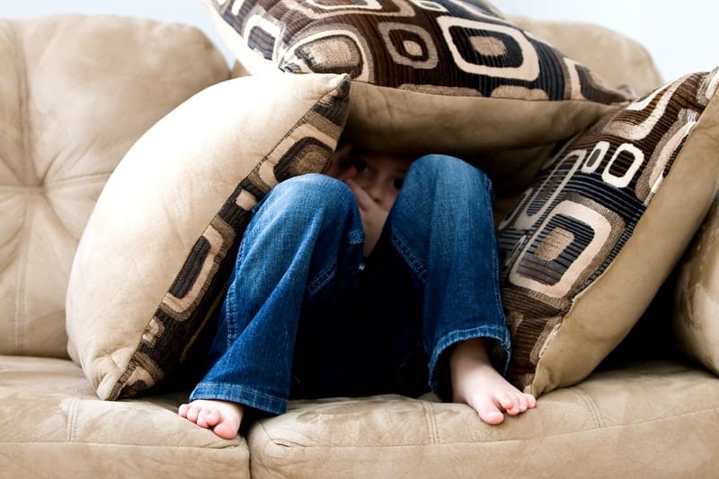 en pojke gömd i kuddar sitter i soffan