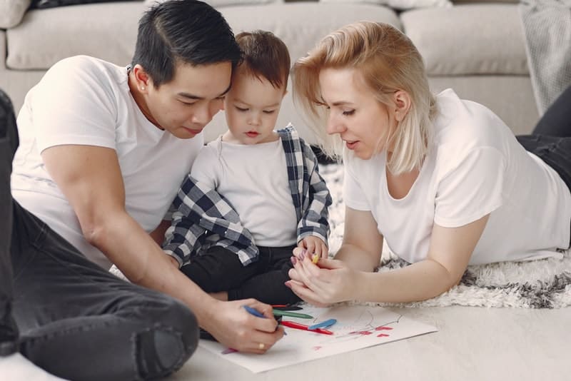 föräldrar med sitt barn sitter på golvet och målar en målarbok