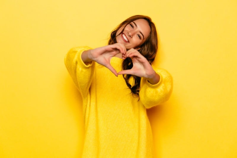 Le ung flicka i gul tröja som visar hjärta med två händer