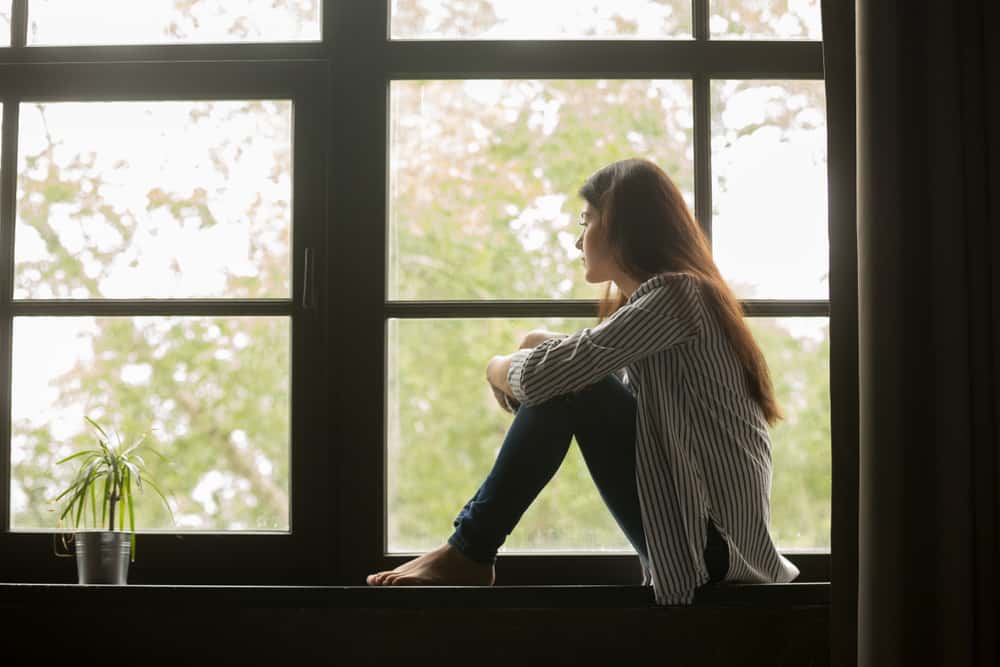 kvinna i djupa tankar som sitter på fönstret och tittar utanför