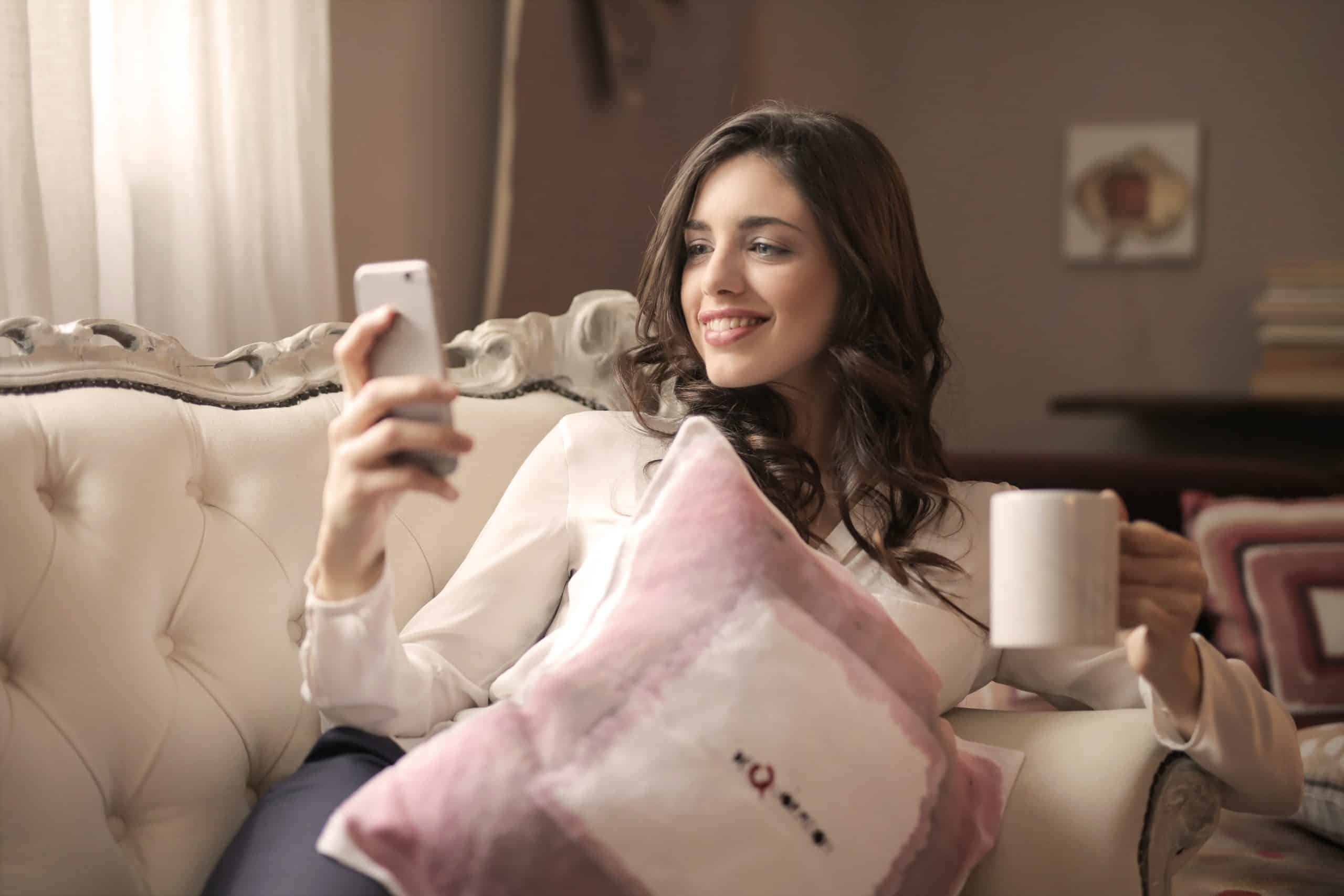 kvinna som håller smarttelefon sitter på tuftad soffa