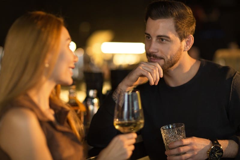 stilig man leende tankeväckande lyssnar på sin vackra kvinna prata medan han njuter av drinkar tillsammans i baren