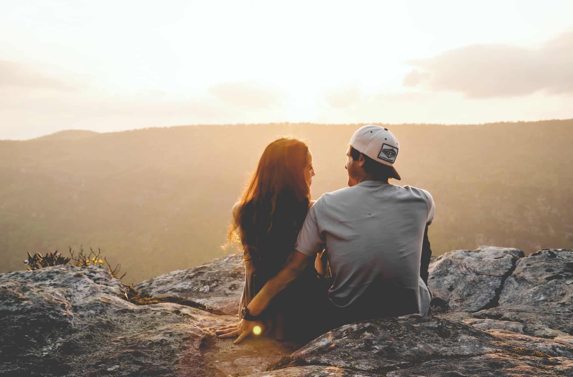 man med mössa och kvinna sitter på klippan njuter av solnedgången