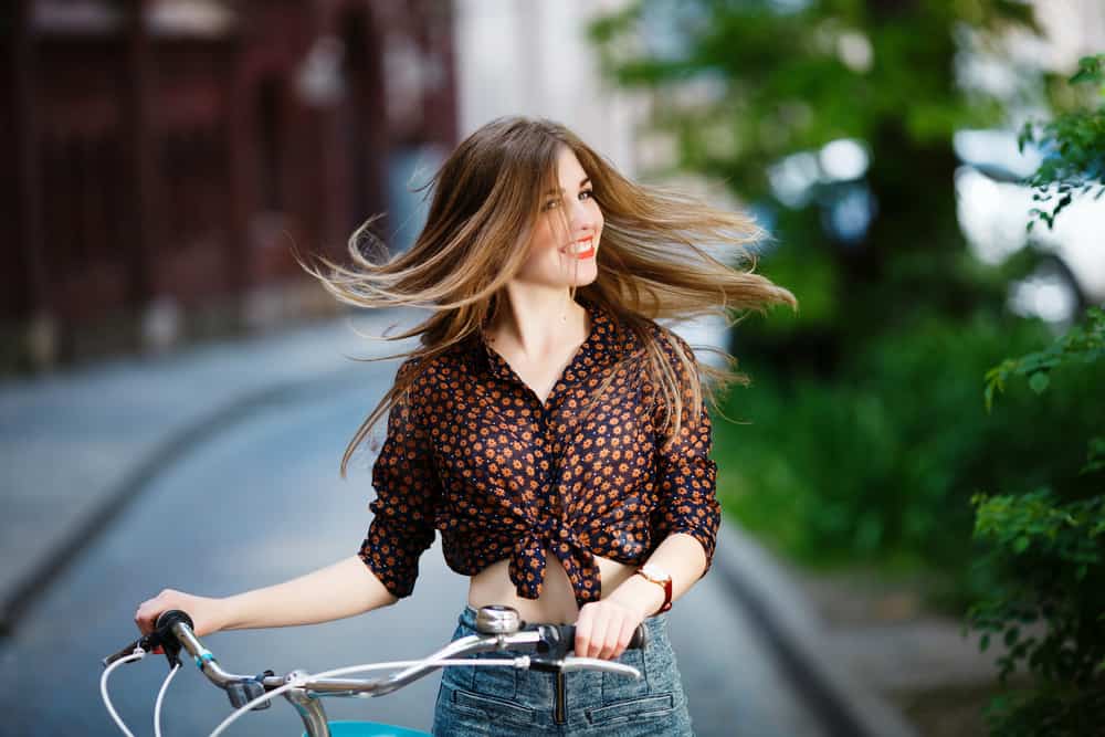 Den nätt ljushåriga flickan står på gatan på blus och shorts med cykeln