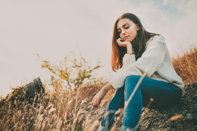 Ledsen ung flicka som utomhus sitter ensam på en sten