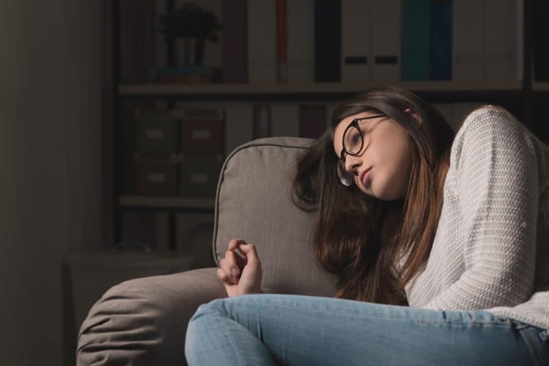 Ledsen ung kvinna med exponeringsglas som hemma sitter på soffan