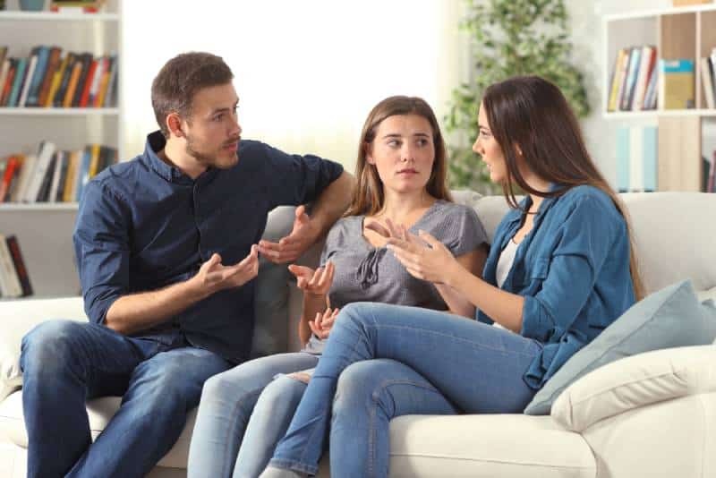 Tre vänliga vänner talar på en soffa i vardagsrummet som sitter på huset