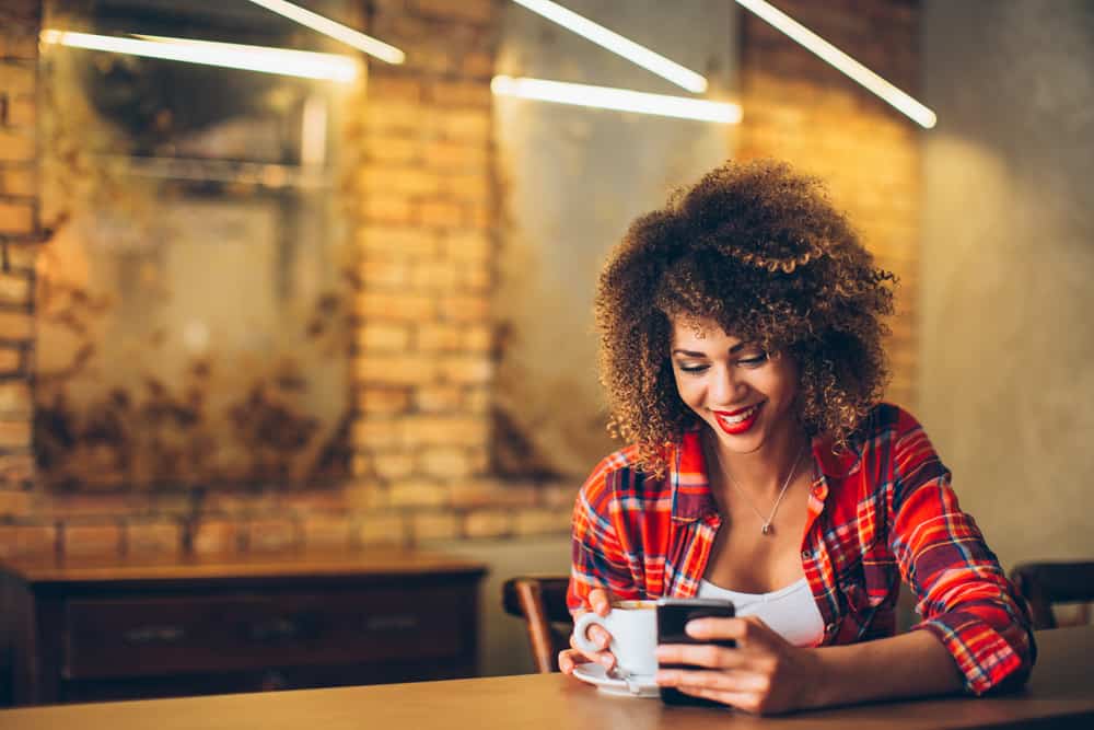 Ung kvinna på kaféet som dricker kaffe och använder mobiltelefonen