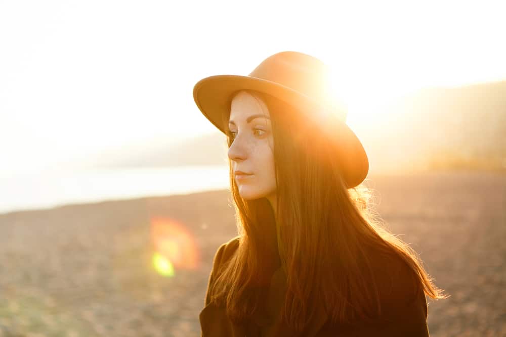 Utomhus profilstående av den charmiga unga kvinnan i kappa och hatt