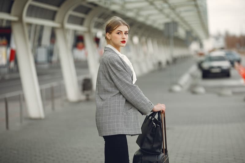 en flicka i en grå kappa står på stationen med en resväska och en väska