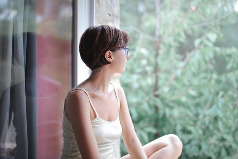en korthårig kvinna i en undertröja sitter vid fönstret och ser ut