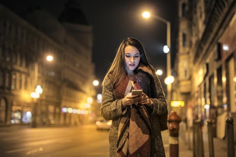 en kvinna går ner på gatan sent på kvällen och skriver i telefon