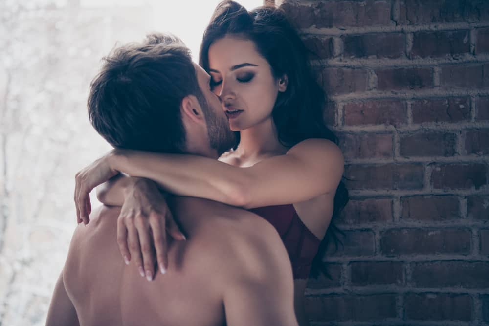 en man kysser en kvinna när han håller fast vid väggen