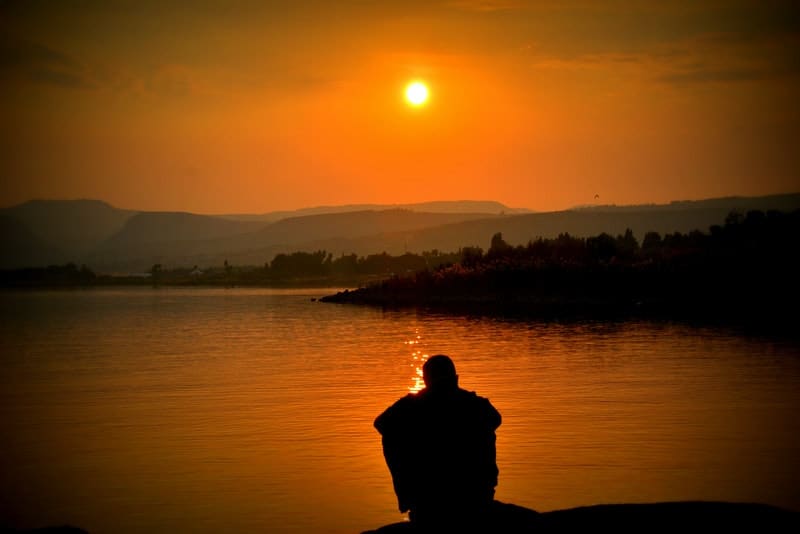 en man sitter vid en sjö och tittar på solnedgången