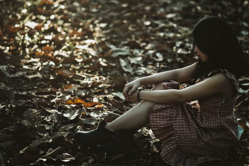 en sorglig kvinna i en rutig klänning sitter på marken i skogen