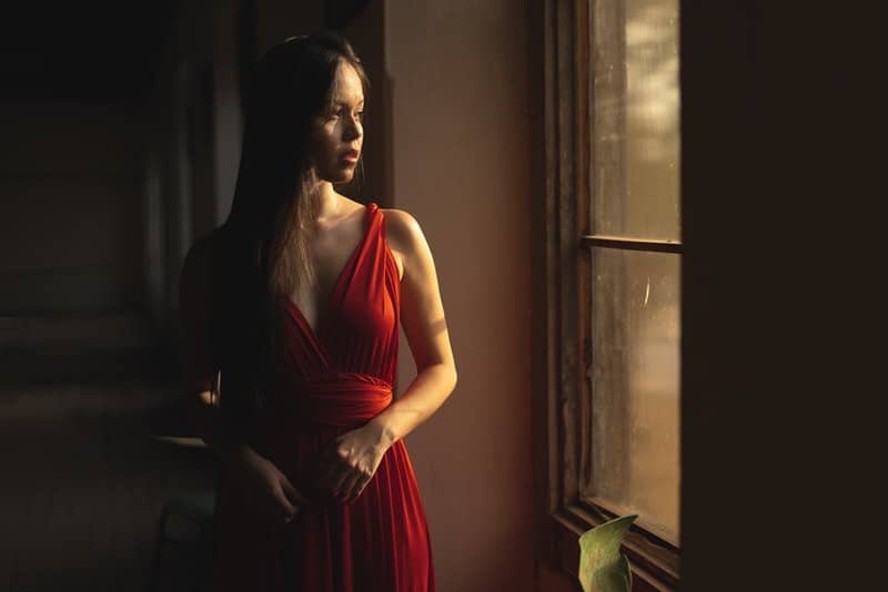 en vacker ledsen kvinna i en röd klänning tänker och tittar ut genom fönstret
