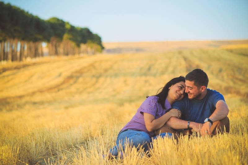 ett älskande par i ett vetefält som sitter i en omfamning