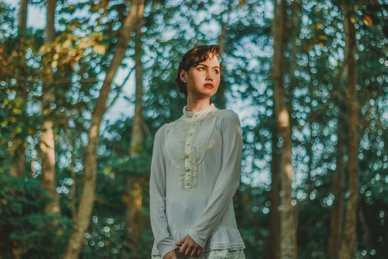 i skogen står en sorglig tjej i en vit klänning