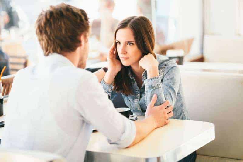 kvinna misstänksamt tittar på mannen medan han håller hennes armar i café