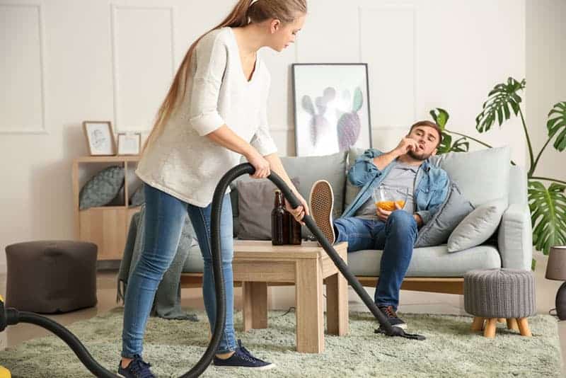 kvinna rengöring golv medan hennes pojkvän tittar på tv