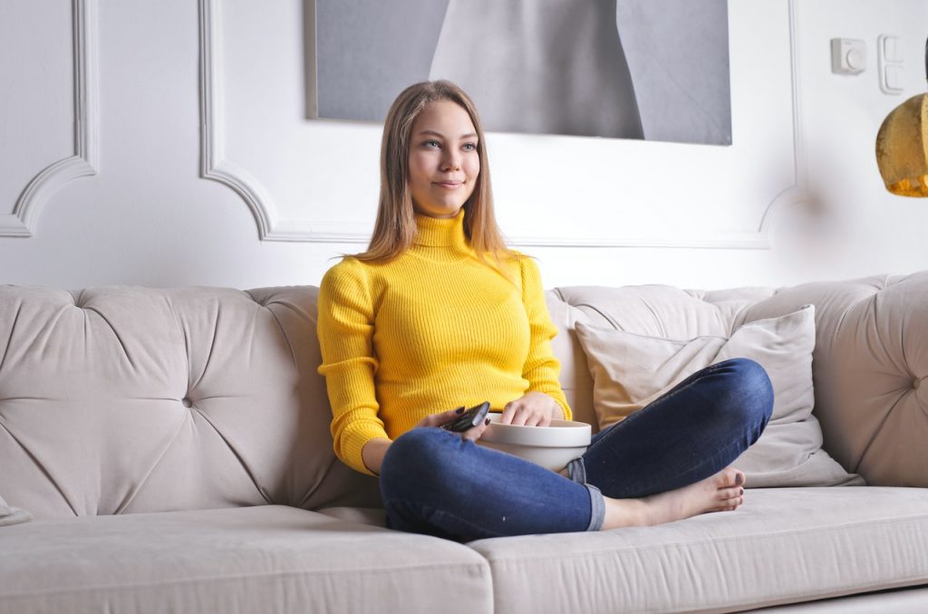 kvinna som sitter på soffan och äter popcorn och tittar på tv